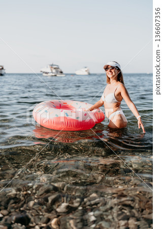 Woman, beach, copy space. Young woman enjoying summer vacation, holding donut float in clear sea water. 136607356