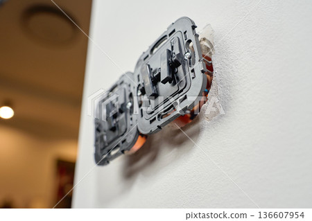 Electrical light switch with exposed wiring and mounting boxes inside white wall. Process of installing electrical sockets. Concept of electrical installation, repair, maintenance and home renovation Electrical light switch with exposed wiring and mounting boxes inside white wall. Process of installing electrical sockets. Concept of electrical installation, repair, maintenance and home renovation 136607954