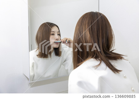 女人一邊刷牙一邊照鏡子 女人一邊刷牙一邊照鏡子 136609885