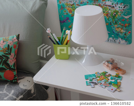 White table in children room near bed. Study area. Education and materials. Furniture and items in modern style. White table in children room near bed. Study area. Education and materials. Furniture and items in modern style. 136610582