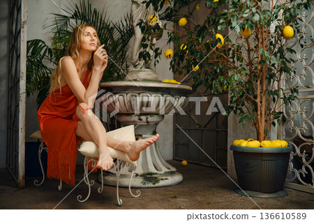 Woman sitting by a lemon tree in a courtyard with stone fountain in daylight Woman sitting by a lemon tree in a courtyard with stone fountain in daylight 136610589