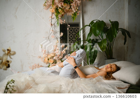 Woman lies on a bed surrounded by plants and flowers in a bright indoor space Woman lies on a bed surrounded by plants and flowers in a bright indoor space 136610603