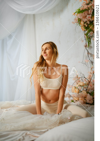 Woman poses on bed surrounded by flowers in a bright room during daytime Woman poses on bed surrounded by flowers in a bright room during daytime 136610621