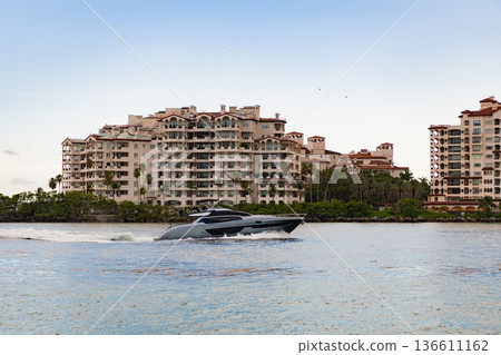 Vacation on summer. Fisher island building. Luxury boat motor yacht. Luxury yacht go to marina. Boating and yachting. Luxury lifestyle. Yacht at Fisher island luxury residential building Vacation on summer. Fisher island building. Luxury boat motor yacht. Luxury yacht go to marina. Boating and yachting. Luxury lifestyle. Yacht at Fisher island luxury residential building 136611162