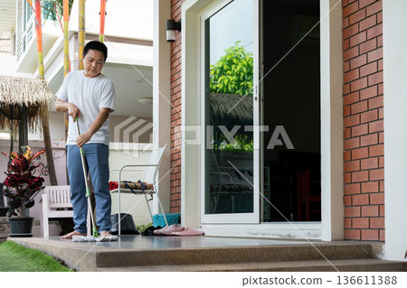 A man is mopping the floor in front of his house on a pleasant, beautiful day. The house is clean and tidy, giving off a relaxing and cozy feeling. A man is mopping the floor in front of his house on a pleasant, beautiful day. The house is clean and tidy, giving off a relaxing and cozy feeling. 136611388
