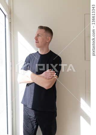 Young man standing by window looking out 136613343