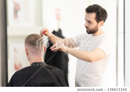 Professional barber cutting male client's hair at salon Professional barber cutting male client's hair at salon 136613348