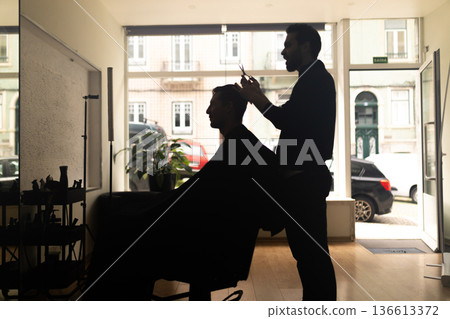 Professional barber cutting male customer hair inside salon Professional barber cutting male customer hair inside salon 136613372