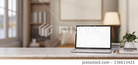 Blank screen laptop and calculator on marble table across sofa and bookshelf in living room 136613421