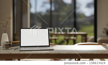 White screen laptop with coffee cup aside vase on marble table in a living room or glass wall cafe. 136613424