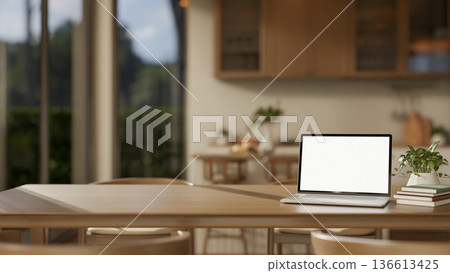 Blank screen laptop with book and potted plant on wooden table across kitchen counter in dining room Blank screen laptop with book and potted plant on wooden table across kitchen counter in dining room 136613425