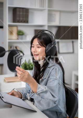 Asian woman wearings headset adjusting mic while hosting a radio show or podcast at home or studio Asian woman wearings headset adjusting mic while hosting a radio show or podcast at home or studio 136613565