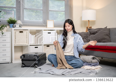 Asian woman looking at cloth packing or organizing luggage for trip on bedroom or living room floor. 136613622