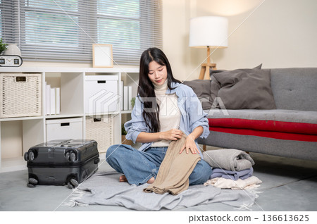 Asian woman folding a cloth packing or organizing luggage for trip on bedroom or living room floor. 136613625