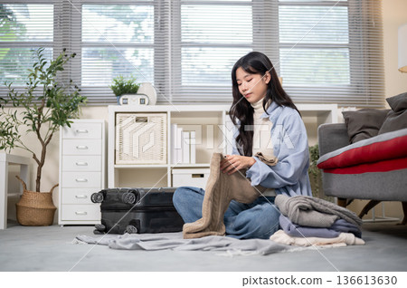 Asian woman folding cloth packing or organizing luggage for a trip on bedroom or living room's floor 136613630