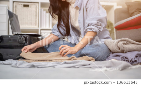 Close up of woman hands folding cloth while packing or organizing luggage in bedroom or living room. 136613643