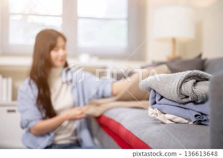 Blurred asian woman folding clothes after laundry on sofa couch in a bedroom or living room at home. Blurred asian woman folding clothes after laundry on sofa couch in a bedroom or living room at home. 136613648