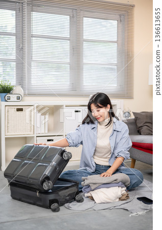 Asian woman opening a luggage to organize or packing while sitting on bedroom or living room's floor 136613655