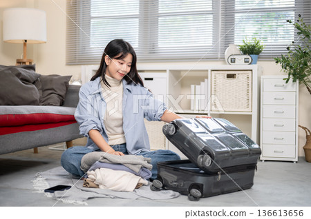 Asian woman opening luggage to organize or packing while sitting on a bedroom or living room's floor 136613656
