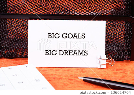A simple desk scene features a card stating big goals big dreams, complemented by a calculator and pen, symbolizing motivation and ambition in daily life A simple desk scene features a card stating big goals big dreams, complemented by a calculator and pen, symbolizing motivation and ambition in daily life 136614704