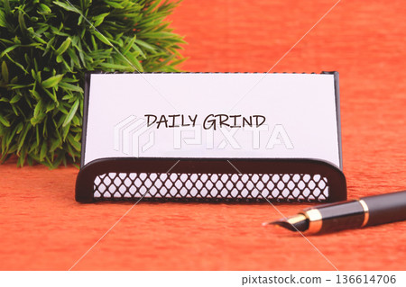 A sleek business card holder displaying the words daily grind sits on a lively orange backdrop, accompanied by a classy fountain pen reflecting professionalism 136614706