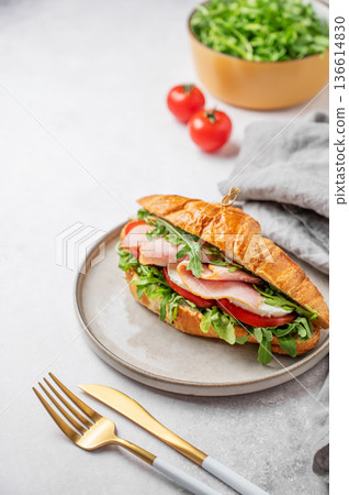Croissant sandwich with ham, mozzarella cheese and arugula on a plate on a light background Croissant sandwich with ham, mozzarella cheese and arugula on a plate on a light background 136614830