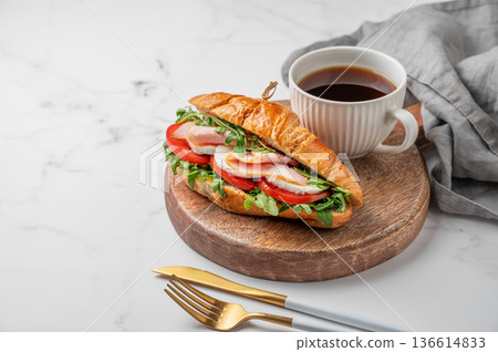 Croissant sandwich with ham, mozzarella cheese, tomato, arugula on a wooden board and cup of coffee Croissant sandwich with ham, mozzarella cheese, tomato, arugula on a wooden board and cup of coffee 136614833