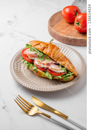 Croissant sandwich with ham, mozzarella cheese and arugula on a plate on a marble background Croissant sandwich with ham, mozzarella cheese and arugula on a plate on a marble background 136614834