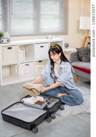 Asian woman putting folded cloth in a luggage while organizing or packing in bedroom or living room. Asian woman putting folded cloth in a luggage while organizing or packing in bedroom or living room. 136615037