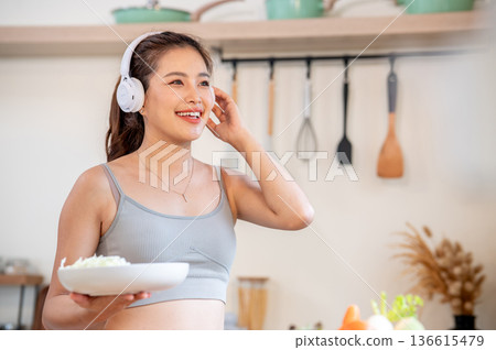 Happy asian woman in sportswear sing song with music in headphone while cooking or eating in kitchen Happy asian woman in sportswear sing song with music in headphone while cooking or eating in kitchen 136615479