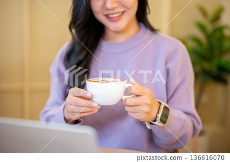 Close up of woman holding coffee cup looking at laptop while sitting at table in cafe or coffee shop Close up of woman holding coffee cup looking at laptop while sitting at table in cafe or coffee shop 136616070