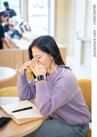 Asian woman closing eyes getting tired after long hours working or study as sitting at table in cafe Asian woman closing eyes getting tired after long hours working or study as sitting at table in cafe 136616096