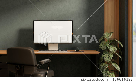 White screen computer on wooden table with leather chair and potted plant in dark green wall room. 136616185