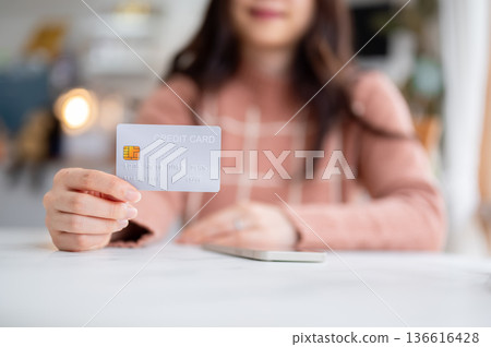 Close up of woman holding phone looking at credit card at table aside glass wall of cafe coffee shop Close up of woman holding phone looking at credit card at table aside glass wall of cafe coffee shop 136616428