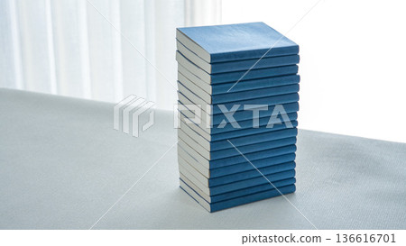 一疊藍色封面的平裝書堆放在一張白桌上。 136616701