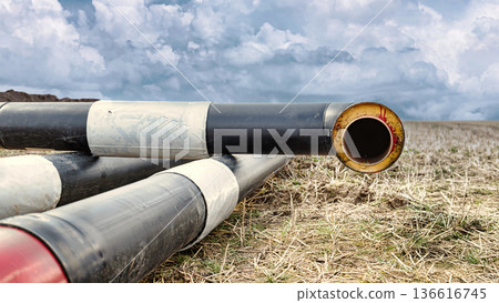 Pipes for the future pipeline are laid out on the ground in an open field under a cloudy sky. The sun is low, indicating sunset Pipes for the future pipeline are laid out on the ground in an open field under a cloudy sky. The sun is low, indicating sunset 136616745
