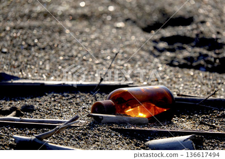 A piece of driftwood on the shore, a small brown bottle shining in the setting sun A piece of driftwood on the shore, a small brown bottle shining in the setting sun 136617494