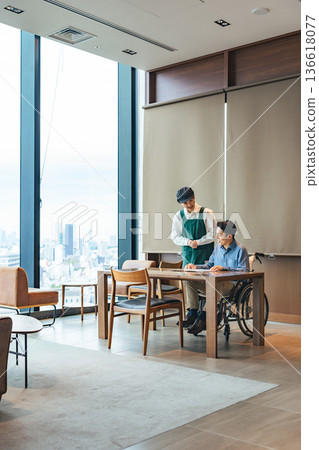 一名餐廳員工為一位坐輪椅的男士服務 一名餐廳員工為一位坐輪椅的男士服務 136618077