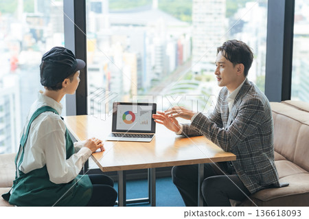 A shop assistant and a business person having a meeting while looking at a laptop A shop assistant and a business person having a meeting while looking at a laptop 136618093