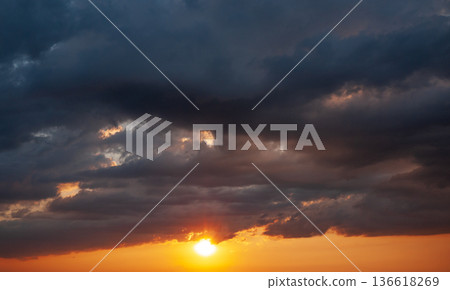 Dramatic dark clouds with sun rays breaking through sunset storm sky Dramatic dark clouds with sun rays breaking through sunset storm sky 136618269