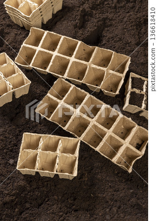 empty cardboard pots for seedlings scattered in a field with fertile brown soil, soil with humus and peat, and paper disposable cups for seedlings in spring 136618410