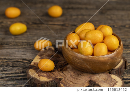 small orange fruits of juicy fresh and fragrant kumquat on a black wooden table, oval kumquat fruit scattered on a black table made of pine wood small orange fruits of juicy fresh and fragrant kumquat on a black wooden table, oval kumquat fruit scattered on a black table made of pine wood 136618432