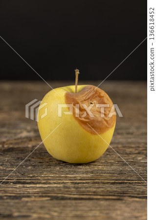 a whole yellow apple with a large orange spot during rotting, one rotting apple on a black wooden table made of pine wood a whole yellow apple with a large orange spot during rotting, one rotting apple on a black wooden table made of pine wood 136618452