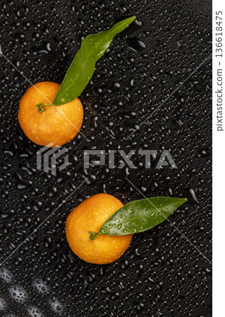 a group of ripe sweet tangerines with green leaves covered with drops of clear water with reflection on a black glass 136618475