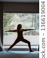 Woman Practicing Yoga Warrior Pose by Window 136619004