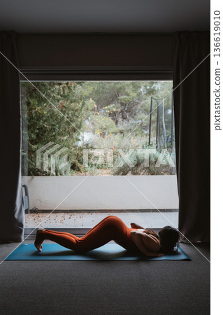 Woman Practicing Yoga on Mat Near Large Window Woman Practicing Yoga on Mat Near Large Window 136619010