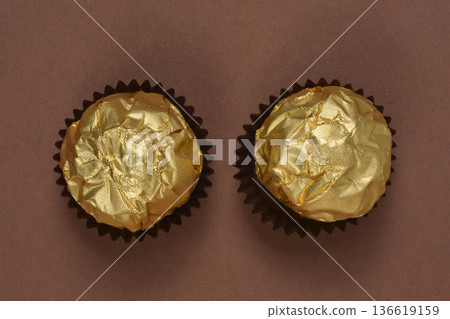 Two chocolate pralines in gold foil on brown background 136619159