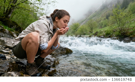 Woman drinking water from mountain river outdoors 136619748