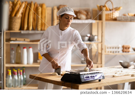 Elderly woman cuts and weighs pieces of dough Elderly woman cuts and weighs pieces of dough 136620634