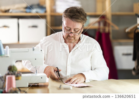 Middle-aged male dressmaker cutting cloth detail in sewing workshop Middle-aged male dressmaker cutting cloth detail in sewing workshop 136620651